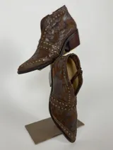 Botas cortas de cuero color chocolate con acabado desgastado y detalle de tachas metálicas. Presentan un taco cuadrado de madera y punta fina.