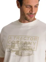 Remera de algodón color beige con cuello redondo y manga corta. Presenta un estampado gráfico en el pecho con la leyenda A TRACTOR COMPANY y la ilustración de un tractor de oruga.