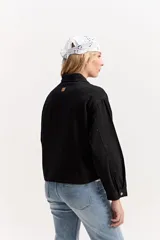 Campera de jean color negro, de calce amplio y largo a la cintura, con cuello alto y cierre frontal con broches a presión.