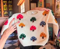 Sweater tejido a mano en lana merino color crema, con cuello redondo y diseño de hongos bordados de colores: rojo, verde, azul y naranja.