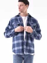 Sobrecamisa a cuadros azul y gris con cuello clásico, cierre frontal con botones, dos bolsillos con solapa abotonada en el pecho y puños abotonados.
