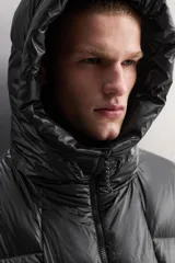 Campera puffer negra con capucha ajustable, cierre frontal con cremallera, bolsillos laterales con cremallera oculta y relleno de plumón y pluma.