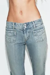 Jeans de tiro bajo con corte flare, confeccionados en denim azul con lavado localizado. Presentan bolsillos de plastrón en el frente, trabillas para cinturón y cierre frontal con cremallera y botones metálicos.