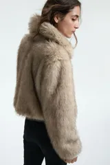 Campera corta de piel sintética en color beige, con cuello redondo, mangas largas y cierre frontal oculto.