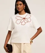 Blusa boxy de mangas cortas color blanco, confeccionada en algodón, con cuello redondo y bordado floral en el frente.