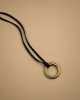 Gargantilla larga con cordón negro y dije de doble argolla metálica en tono dorado.