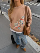 Buzo de algodón color tostado, de corte cropped y estilo oversize. Presenta cuello redondo, mangas largas con puños ajustados y elástico en la cintura. Destaca por una estampa exclusiva de flores en el frente y en una de las mangas.
