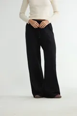 Pantalón negro de corte amplio y tiro alto, confeccionado en tejido de punto con costuras verticales decorativas en el frente y cintura elástica con cordón ajustable.