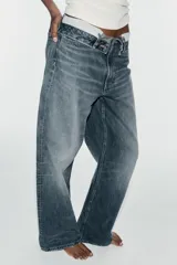 Jeans de mezclilla de tiro medio, corte wide leg y diseño relaxed. Presenta detalles rotos y desgastados en las piernas, y una cinturilla doblada superpuesta con trabillas y cierre frontal con cremallera y botón metálico.