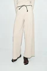 Pantalón de tiro alto y pierna recta, confeccionado en tejido piqué color beige. Presenta cintura elástica y un cinturón fino a contraste en color negro con detalle de pieza metálica central.