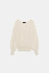 Blusa de punto color beige con cuello barco, manga larga abullonada con puños ajustados y detalles fruncidos en la parte delantera.