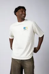 Remera de corte oversize color beige, confeccionada en algodón grueso. Presenta una estampa frontal pequeña con diseño artístico abstracto en tonos azules y amarillos.