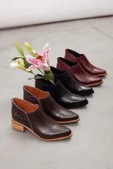 Botines de cuero negro con diseño moderno, silueta estilizada y punta fina. Cuentan con un corte en V en el lateral y tacón cuadrado de altura media.
