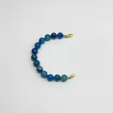 Pulsera de cuentas esféricas de ágata azul de 10 mm, unidas mediante nudos de hilo azul. Presenta cierre de mosquetón y terminales con baño de oro.