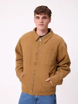 Campera de lona color tostado con cierre frontal, cuello camisero y bolsillo en el pecho. Presenta un diseño de estilo workwear con interior forrado.