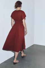 Vestido midi de color bordó con escote en pico y mangas cortas. Presenta un diseño con pinzas, cierre frontal con botones ocultos y un cinturón fino tipo cordón en el mismo tejido para ajustar a la cintura.