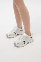 Zapatilla deportiva de estilo urbano en color blanco con detalles metalizados plateados y acentos en negro. Presenta una combinación de malla transpirable y paneles sintéticos, con suela robusta y cordones al tono.