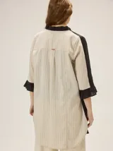 Camisa de lino de silueta relajada y largo irregular, color beige, con cuello mao, botones frontales a contratono y mangas tres cuartos terminadas en volados.