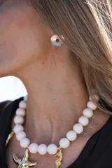 Collar de grandes cuentas esféricas de color blanco, con dijes colgantes dorados en forma de estrella de mar y caballito de mar.