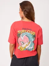 Remera coral cropped, de manga corta, con estampa trasera colorida de un perro surfeando y el texto "Rusty County Surf Club".
