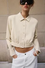 Camisa crop de manga larga con cuello solapa y cierre frontal de botones, confeccionada en tejido sintético con efecto piel color beige.