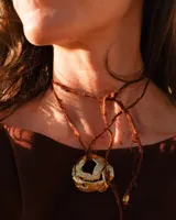 Collar artesanal con dije de flor en bronce o alpaca, suspendido en un cordón de seda natural teñido a mano. El diseño permite atarse con un moño, ofreciendo versatilidad para lucirlo de distintas formas.