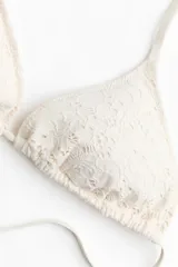 Top de bikini triangular color beige con textura de encaje, con copas con relleno extraíble y tiras para anudar al cuello y la espalda.