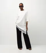 Remera oversized de algodón color blanco, con cuello redondo, mangas cortas amplias y detalle de encaje asimétrico en el ruedo.