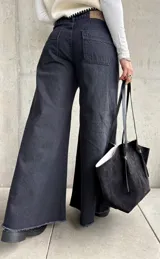 Jean de corte oxford y tiro medio, color negro lavado. Presenta diseño de pierna ancha con costuras verticales decorativas y ruedo deshilachado.