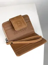 Billetera pequeña de cuero color marrón claro con paneles frontales de pelo natural. Presenta un cierre de solapa con broche y un logo grabado de un búho. Incluye una correa de muñeca extraíble.