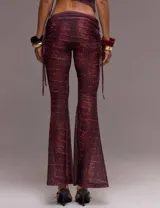Conjunto de dos piezas compuesto por un top de manga corta con recortes, detalle metálico frontal y cuello tipo mao, y un pantalón de tiro bajo con corte flare. Ambas prendas presentan un estampado efecto piel de cocodrilo en tonos vino.