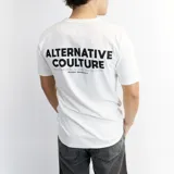 Remera blanca de algodón con cuello redondo y mangas cortas. Estampado en la espalda con la frase "ALTERNATIVE COULTURE" en letras grandes y debajo "PARIS NEW YORK MADRID TOKYO MILAN DUKON ORIGINALS" en letras más pequeñas.