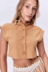 Camisa corta color ocre de lino, con cuello clásico, cierre frontal con botones y mangas cortas con solapas.