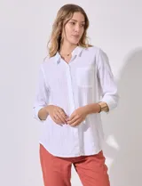 Camisa blanca de corte clásico con textura de líneas verticales, cuello con solapa, cierre frontal con botones y bolsillo en el pecho. Presenta mangas tres cuartos regulables con presilla y botón.