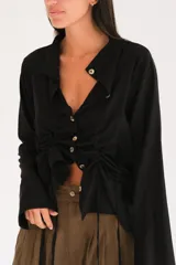 Camisa de lino blanca con botones frontales, cuello clásico, mangas largas y cordones ajustables para fruncir en la cintura.