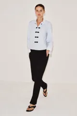 Camisa de algodón con cuello solapa y puños en color blanco a contraste. Presenta cierre frontal con alamares negros y bajo asimétrico redondeado.