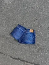 Short de jean azul de tiro bajo, con bolsillos traseros appliqués que presentan un diseño de estrella acolchada. Incluye etiqueta de cuero sintético naranja en la parte posterior de la cintura.