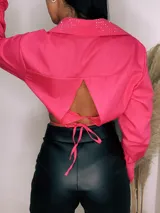 Camisa cropped negra con cuello clásico, mangas largas con puños abotonados y cierre frontal con botones. Presenta detalle de tachas plateadas en el cuello.