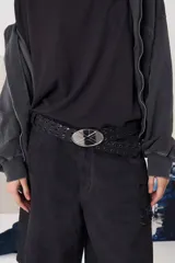 Cinturón de cuero negro con perforaciones decorativas a lo largo de toda la tira y hebilla metálica ovalada con detalle central.