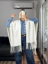 Poncho de tejido suave color blanco, con diseño abierto y flecos en el ruedo inferior.