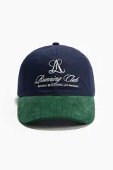 Gorra confeccionada en sarga de algodón azul marino con visera de pana verde oscuro. Presenta bordado frontal con texto y monograma en hilo blanco.