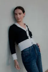 Saco tipo cardigan bicolor con diseño de bloques en blanco y negro, cuello en V, cierre frontal con botones y mangas largas con puños ajustados.