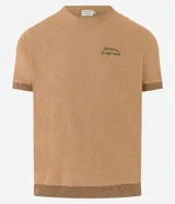Remera de manga corta color marrón claro, confeccionada en algodón, poliéster, viscosa, elastano y poliamida. Presenta cuello redondo, corte regular y estampa frontal con palmeras y texto "Savane Tropicale".
