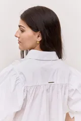 Camisa azul marino de cuello clásico, mangas abullonadas a tres cuartos y detalle fruncido en el frente. Presenta una silueta amplia y diseño corto con vuelo en el ruedo.