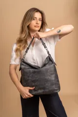 Cartera tipo bandolera de gran tamaño, confeccionada en cuero sintético con acabado desgastado. Cuenta con una asa corta fija, una correa larga regulable y extraíble, y una placa metálica con la marca en la parte frontal.