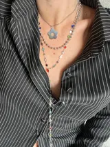 Set de tres collares plateados de diferentes largos. El más corto es tipo choker, el segundo tiene un dije de flor y el más largo es tipo corbatín con piedras de colores.