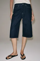 Bermuda de denim azul oscuro de tiro medio y corte recto, perteneciente a la ZARA Woman Collection. Cuenta con diseño de cinco bolsillos, trabillas para cinto y cierre frontal con cremallera y botón metálico.