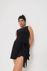 Vestido corto deportivo negro, sin mangas, con cuello redondo y detalle de lazo anudado en la cintura. Presenta el logo 'bk.' estampado en blanco en el pecho.