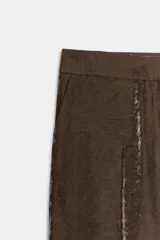 Pantalón de tiro alto con pernera recta, confeccionado en tejido con acabado brillante y textura arrugada. Presenta bolsillos delanteros y cierre frontal con cremallera, botón interior y gancho.