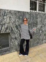 Conjunto compuesto por remera de manga larga oversize a rayas horizontales blancas y negras con escote bote, y pantalón negro de corte flared.